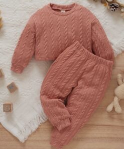 A soft, bick red cable knit loungewear set for babies and toddlers, including a long-sleeved jumper and matching joggers, laid flat on a white blanket with wooden toys.