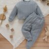 A soft, dusty blue cable knit loungewear set for babies and toddlers, including a long-sleeved jumper and matching joggers, laid flat on a white blanket with wooden toys.