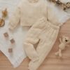 A soft, khaki cable knit loungewear set for babies and toddlers, including a long-sleeved jumper and matching joggers, laid flat on a white blanket with wooden toys.