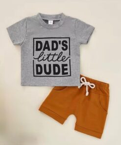 A baby and toddler boy's two-piece set, featuring a grey marl cotton t-shirt with "Dad's Little Dude" in black print and a pair of rich tan shorts with a drawstring.